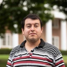 Man with short dark hair wearing multi color striped polo shirt in front of Old Centre